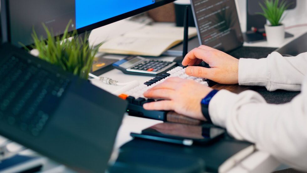 A person typing on a keyboard at a desk with a calculator and smartphone, illustrating efficient data processing for optimizing credit card processing fees with Optimized Payments.